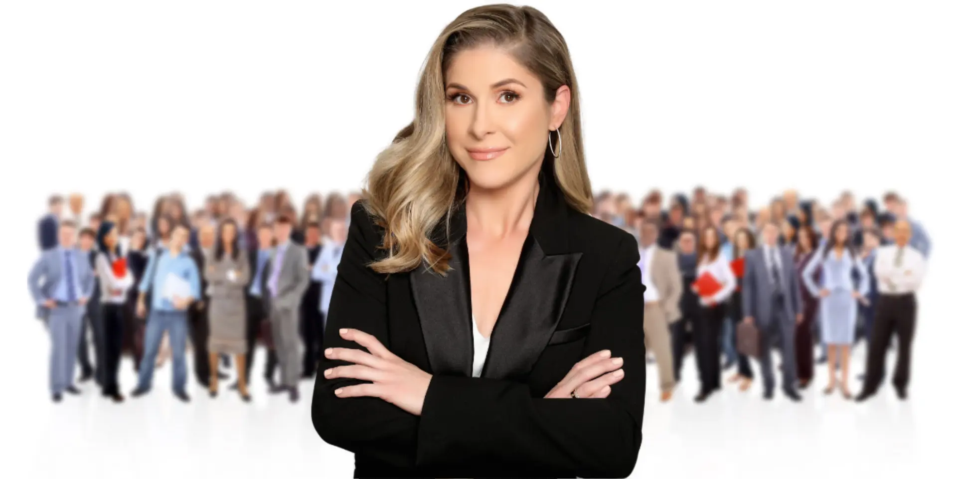 Confident woman in a black blazer stands in front of a large, blurred group of professionally dressed people.
