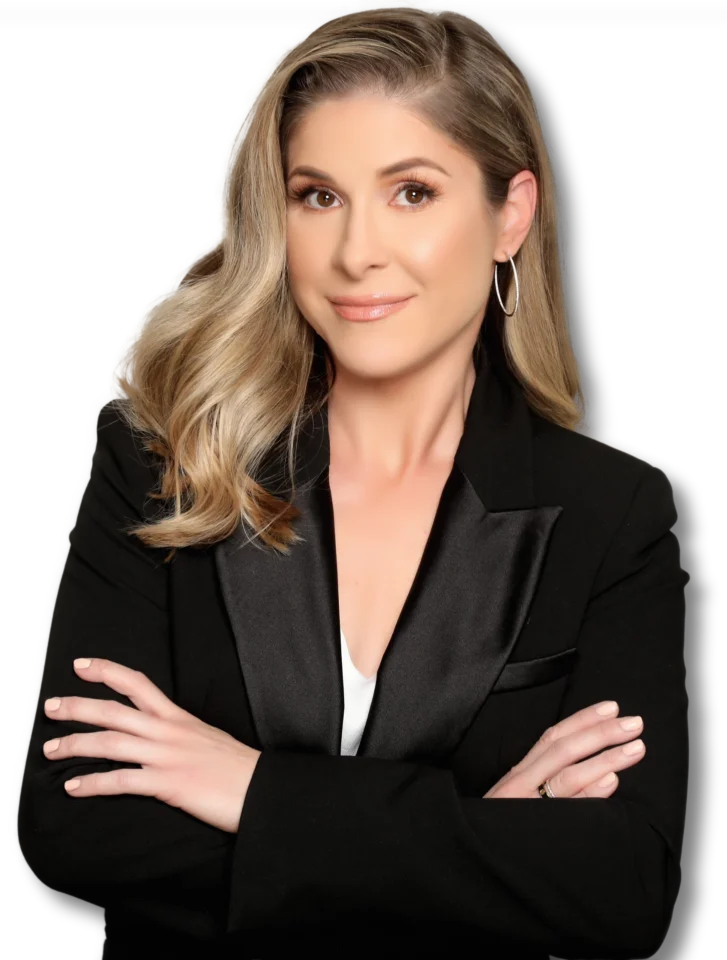 Woman with long blonde hair in a black blazer, arms crossed, smiling at the camera against a light background.