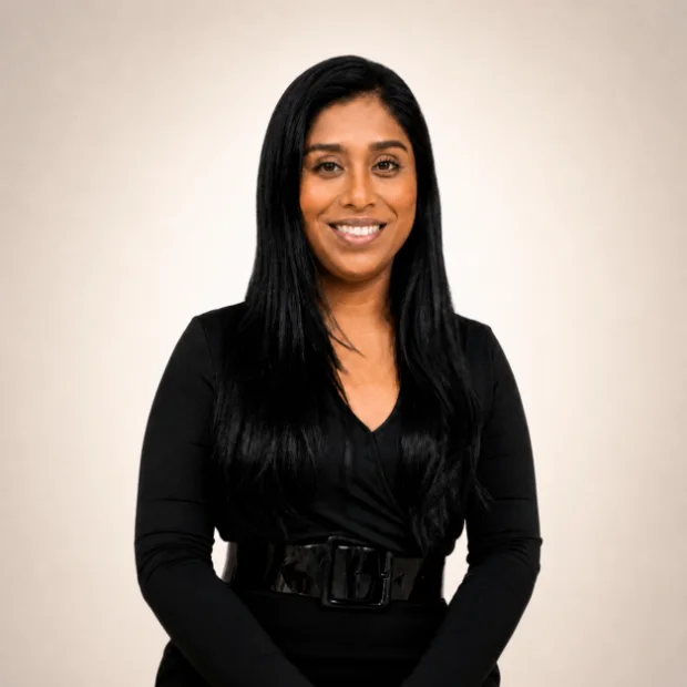 Woman with long black hair, wearing a black outfit, smiling and posing against a plain light background.